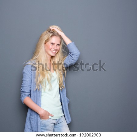 Portrait of a beautiful young woman smiling with hand in hair on gray background
