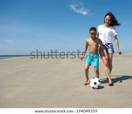 Young single mother playing with ball together with son on the beach
