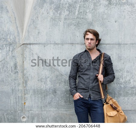Portrait of a cool guy posing with leather travel bag outdoors