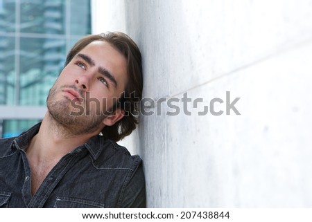 Close up portrait of a young man leaning against wall and looking up