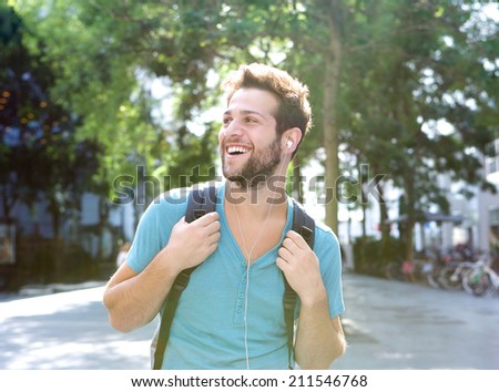 Close up portrait of a happy young man traveling with backpack and earphones