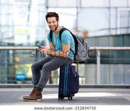 Portrait of a young man sitting on suitcase and sending text message