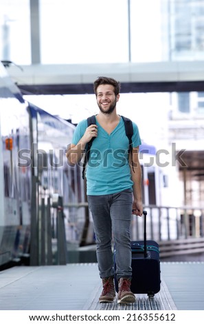Full length portrait of a happy young man walking with suitcase at train station