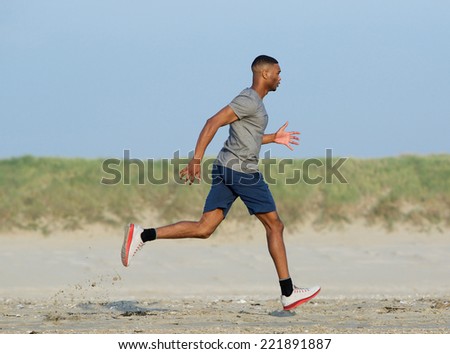 Side view of an african american man jogging at the beach