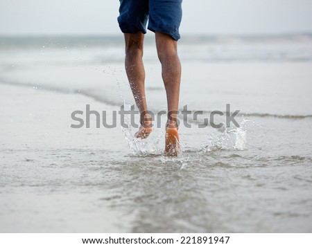 Close up rear view of a man running with bare feet in water by the beach
