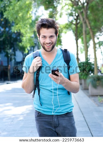 Portrait of a happy young man walking outdoors with mobile phone and earphones