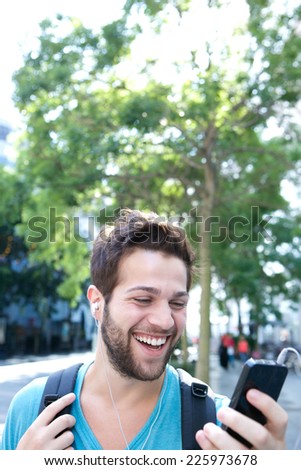 Close up portrait of a young man smiling with backpack and looking at mobile phone
