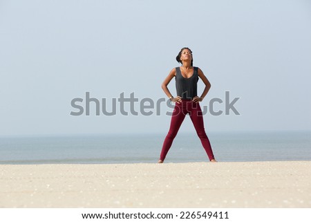 Portrait of an african woman doing yoga breathing exercise with hands on hip at the beach