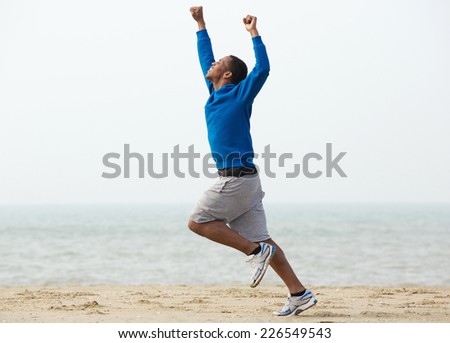 Young black man running at the beach with arms raised in victory
