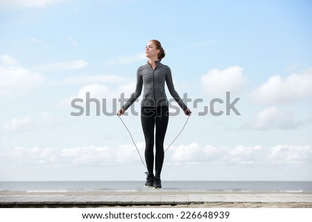 Sporty woman warming up with jump rope outdoors