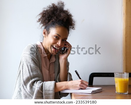 Close up portrait of a happy young woman calling by phone and writing in notebook