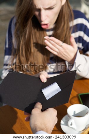 Close up portrait of a shocked young woman looking at restaurant bill