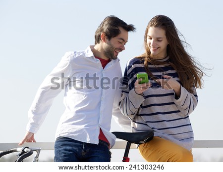 Close up portrait of a happy couple standing outside and looking at text message on cell phone