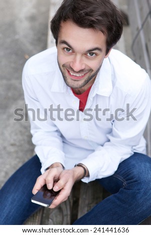 Portrait of a young man smiling outdoors with mobile phone