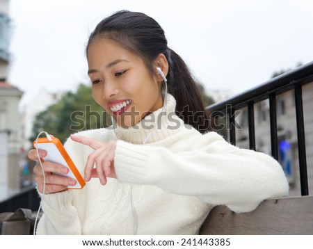 Close up portrait of a young asian woman smiling with cellphone and earphones