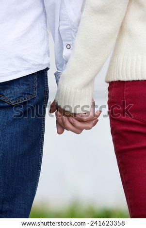 Back view of boyfriend and girlfriend holding hands outdoors
