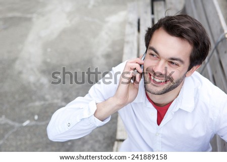Close up portrait of a young man smiling and calling by mobile phone outdoors