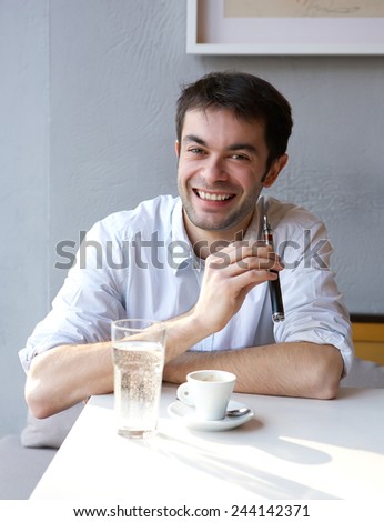 Portrait of a smiling young man sitting indoors with e cigarette