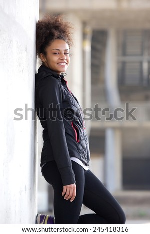 Portrait of a smiling sports woman relaxing outdoors, leaning against wall