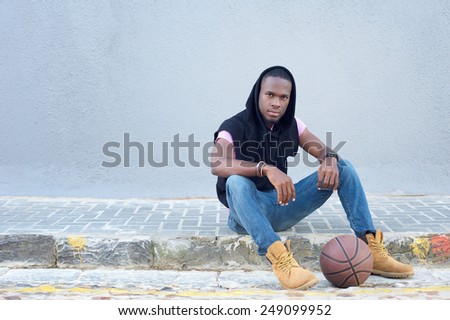 Portrait of a cool young guy sitting on sidewalk with basketball