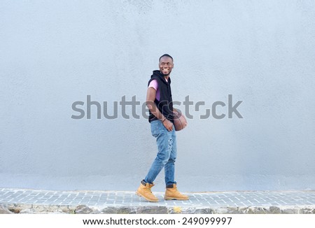 Portrait of a young man walking on sidewalk with basketball