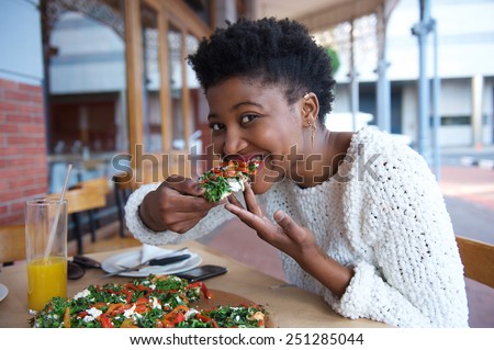 Close up portrait of a young black woman eating vegetarian pizza