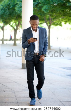Full body portrait of a handsome man walking and sending text message on cellphone