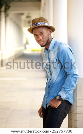 Side portrait of a relaxed young man with hat leaning on wall outdoors