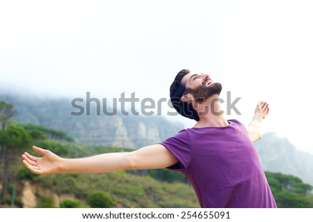 Portrait of a happy carefree man smiling with arms open outdoors