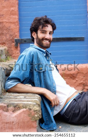 Side portrait of a handsome young man with beard sitting on step