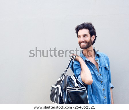 Young smiling man with beard holding travel bag and looking over shoulder