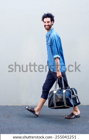 Full length portrait of a happy modern man walking and holding travel bag
