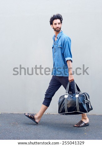 Full length side view portrait of a young man walking with travel bag