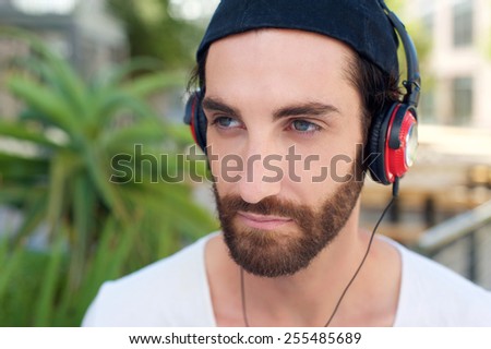 Close up portrait of a young man with beard listening to music on headphones
