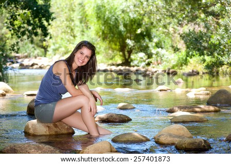 Portrait of a happy young woman sitting by stream with feet in water