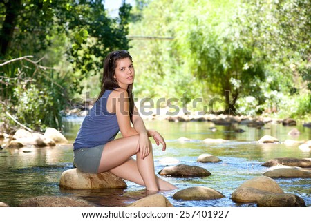 Young woman sitting on rock by a stream with bare feet in water