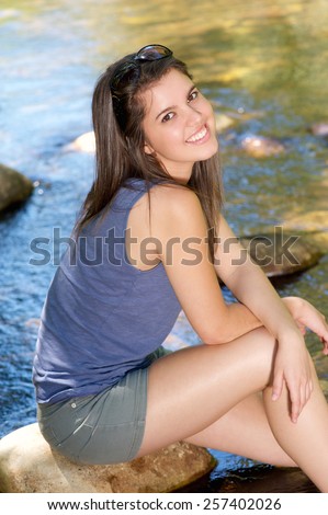 Portrait of a happy girl sitting next to stream with feet in water