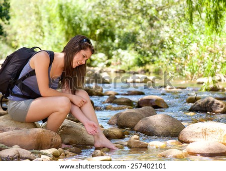 Happy young woman sitting by stream with backpack