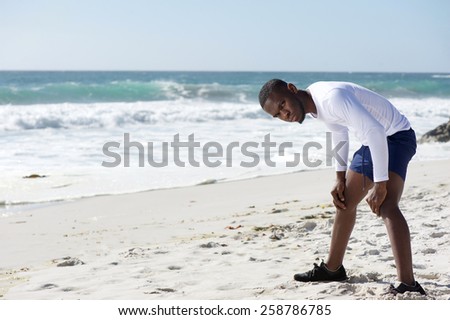 Young african american man standing on beach with hands on knees