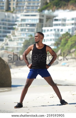 Full body sporty man standing on beach in sportswear