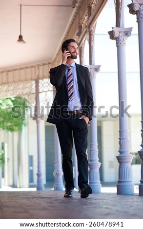 Full body portrait of a happy businessman walking and talking on mobile phone