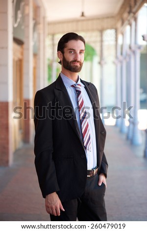 Portrait of a young businessman with beard and formal suit standing outside