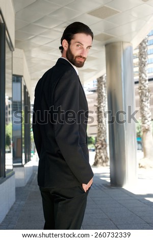 Portrait from behind of a male fashion model in black business suit standing outdoors