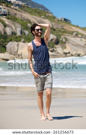 full body happy young man on vacation walking barefoot on isolated beach