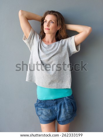 Portrait of a relaxed woman standing against gray background with hands behind head