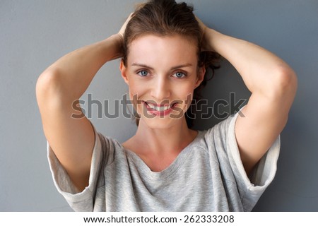 Close up portrait of a happy mid adult woman smiling with hands in hair against gray background