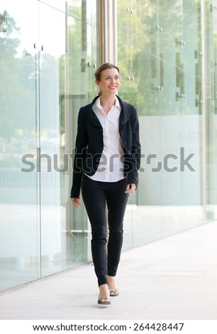 Full body portrait of a happy business woman walking outside office building