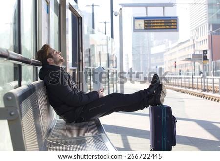 Side portrait of a smiling young man sitting with bag waiting for train