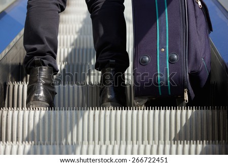 Portrait from behind of a man standing on escalator with travel bag