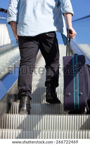 Portrait of back of man walking up escalator with travel bag